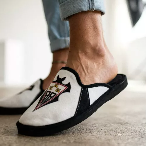 Par de zapatillas de casa del Celta de Vigo sobre una alfombra de yute frente a un sofá beige, estilo de fotografía de catálogo de hogar.